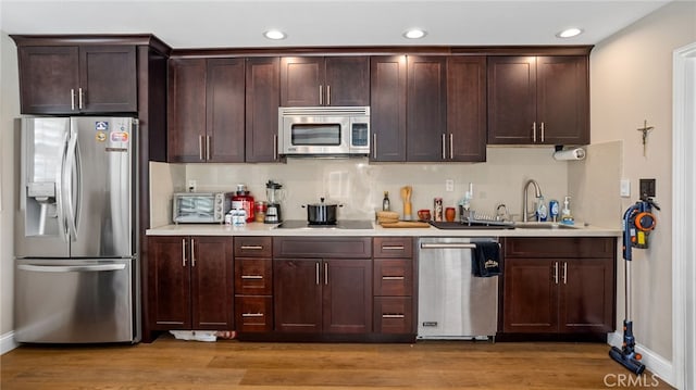 kitchen featuring appliances with stainless steel finishes, light countertops, baseboards, dark brown cabinetry, and light wood-type flooring