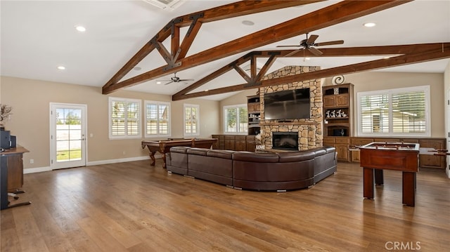 living room featuring a ceiling fan, wood finished floors, baseboards, a stone fireplace, and healthy amount of natural light