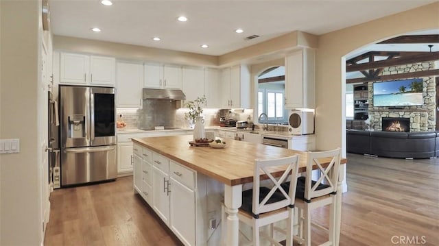 kitchen with stainless steel fridge, under cabinet range hood, wood counters, light wood-style flooring, and white cabinets