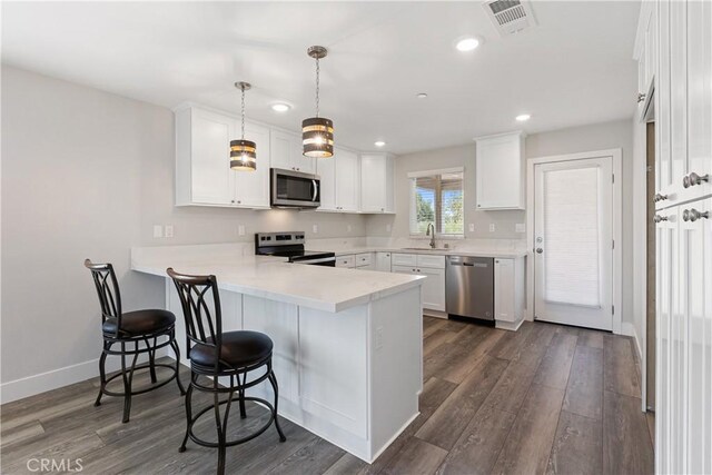 6018 William St, Riverside, CA 92504 - kitchen featuring stainless steel appliances, a peninsula, dark wood-style flooring, white cabinetry, and a breakfast bar area