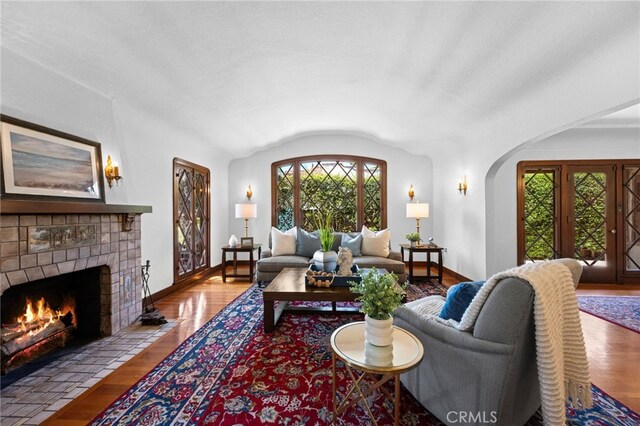 2415 N French St, Santa Ana, CA 92706 - living room with baseboards, lofted ceiling, arched walkways, a tile fireplace, and wood finished floors