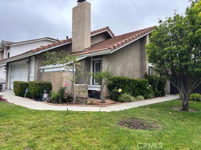 view of front facade with a chimney, a front lawn, stucco siding, and a tiled roof