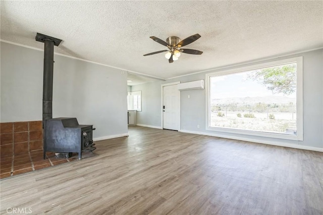 1561 Old Woman Springs Rd, Yucca Valley, CA 92284 - unfurnished living room with a wood stove, wood finished floors, a wall mounted air conditioner, ceiling fan, and a textured ceiling