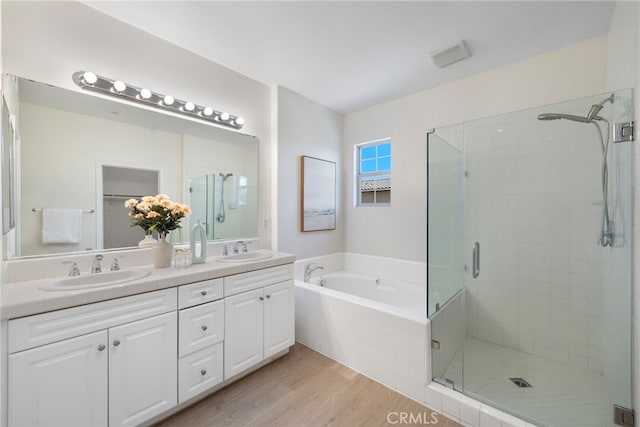 bathroom featuring a shower stall, wood finished floors, a garden tub, and double vanity