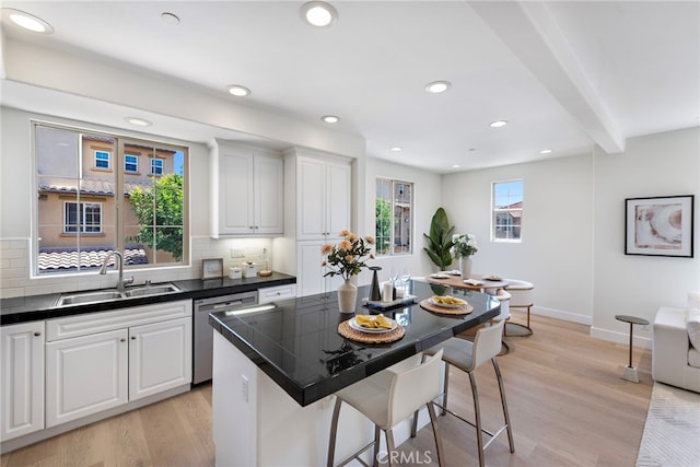 kitchen with a sink, dishwasher, a breakfast bar area, dark countertops, and backsplash