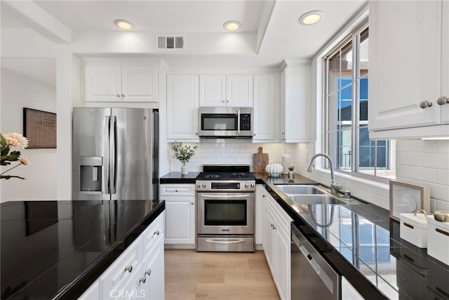 kitchen featuring appliances with stainless steel finishes, a sink, white cabinetry, light wood-type flooring, and recessed lighting