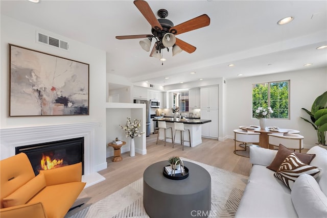 living room featuring light wood-style floors, recessed lighting, ceiling fan, a glass covered fireplace, and baseboards