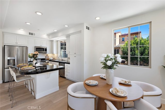 kitchen featuring stainless steel appliances, dark countertops, white cabinetry, light wood-type flooring, and a breakfast bar