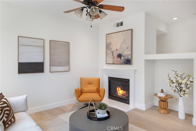 living area with light wood finished floors, a glass covered fireplace, ceiling fan, baseboards, and recessed lighting