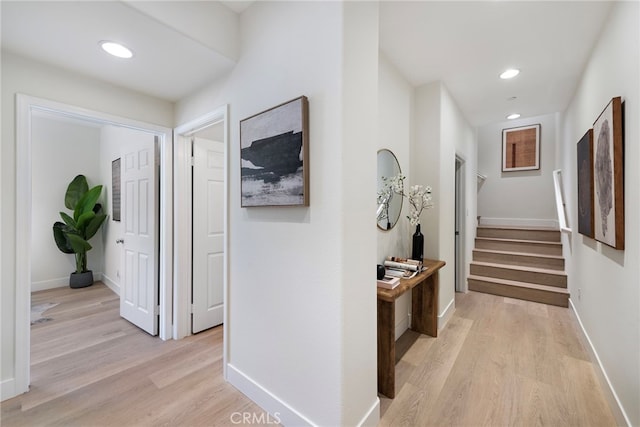 hallway with light wood-type flooring, baseboards, recessed lighting, and stairway