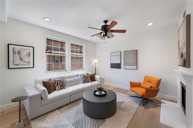 living room featuring wood finished floors, baseboards, recessed lighting, ceiling fan, and a fireplace