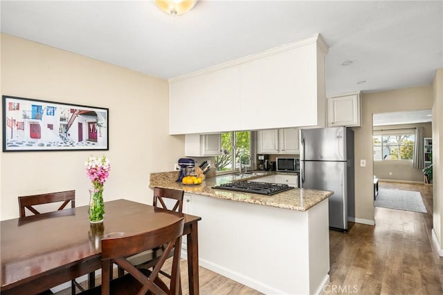 25388 Via Verde Unit 4, Lake Forest, CA 92630 - kitchen with stainless steel appliances, a peninsula, a sink, wood finished floors, and light stone countertops
