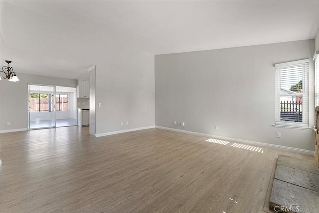 unfurnished living room featuring light wood-style flooring, baseboards, and a chandelier