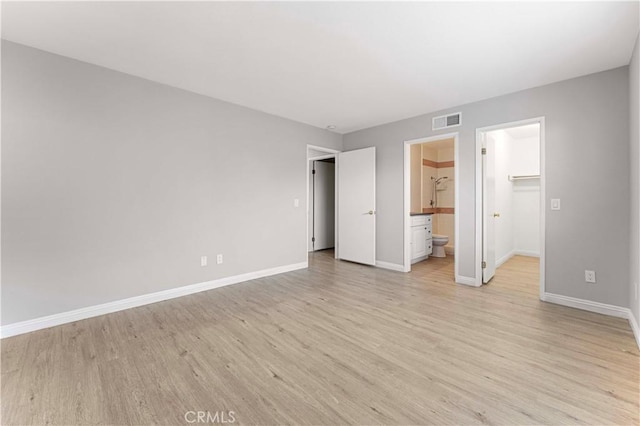 unfurnished bedroom with light wood-style floors, baseboards, a walk in closet, a closet, and connected bathroom