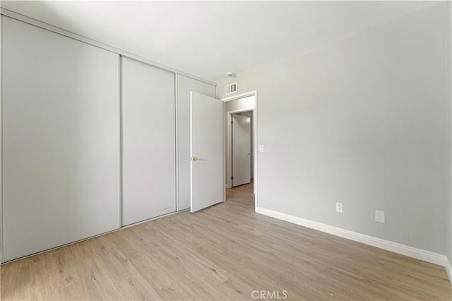 unfurnished bedroom featuring light wood-style flooring, a closet, and baseboards