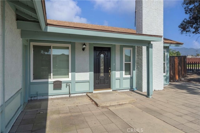 doorway to property with fence, a chimney, brick siding, stucco siding, and a porch