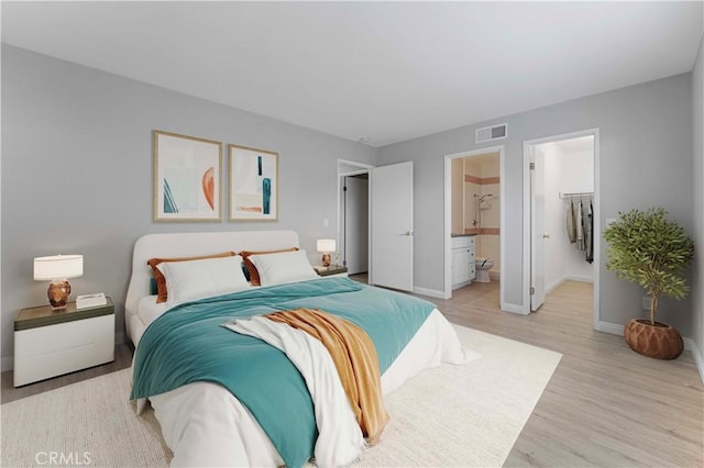 bedroom featuring baseboards, light wood finished floors, and a walk in closet