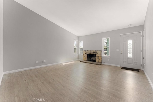 unfurnished living room featuring light wood-style floors, a stone fireplace, vaulted ceiling, and baseboards