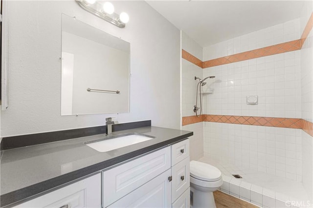 full bath with tiled shower, toilet, and vanity