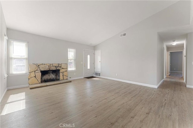 unfurnished living room featuring light wood-style floors, a stone fireplace, vaulted ceiling, and baseboards
