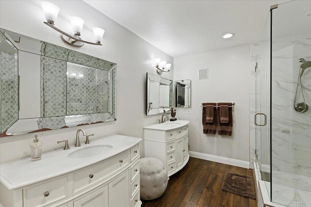 bathroom with a marble finish shower, wood finished floors, two vanities, and baseboards