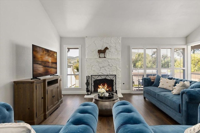 living room with a stone fireplace, dark wood-type flooring, and baseboards