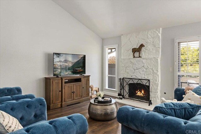 living area with dark wood finished floors, a stone fireplace, and vaulted ceiling