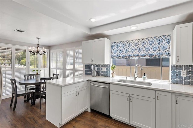 kitchen featuring stainless steel dishwasher, a sink, a chandelier, a peninsula, and decorative backsplash