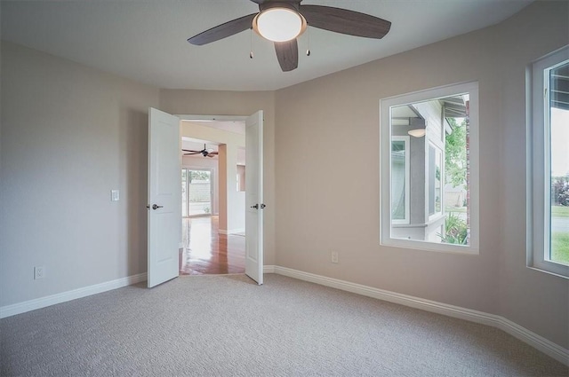 spare room with a ceiling fan, plenty of natural light, light carpet, and baseboards