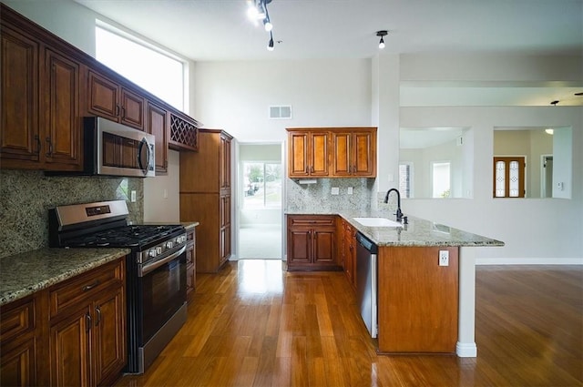 kitchen featuring appliances with stainless steel finishes, a sink, a peninsula, wood finished floors, and a high ceiling