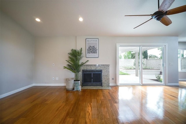 unfurnished living room with plenty of natural light, a premium fireplace, wood finished floors, baseboards, and recessed lighting