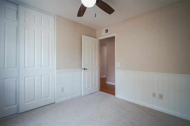 unfurnished bedroom featuring wainscoting, carpet floors, a closet, and ceiling fan