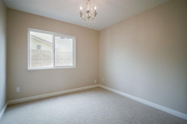 carpeted empty room with a chandelier and baseboards