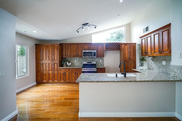 kitchen featuring appliances with stainless steel finishes, a sink, lofted ceiling, a peninsula, and tasteful backsplash