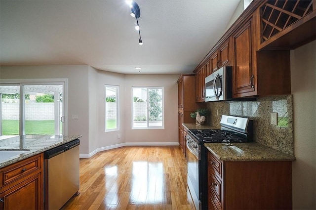 kitchen featuring stainless steel appliances, baseboards, light wood-type flooring, decorative backsplash, and dark stone countertops