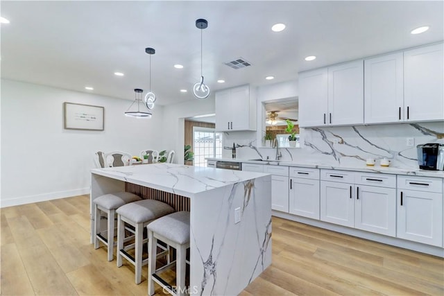 10612 Ketch Ave, Garden Grove, CA 92843 - kitchen featuring white cabinets, a breakfast bar, light wood finished floors, a kitchen island, and light stone counters