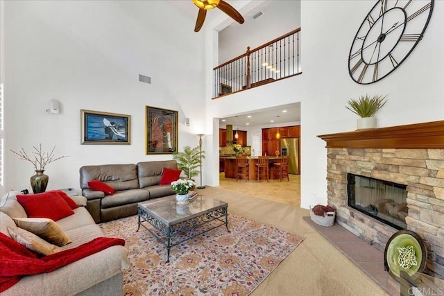 living area with light carpet, ceiling fan, a stone fireplace, and a high ceiling