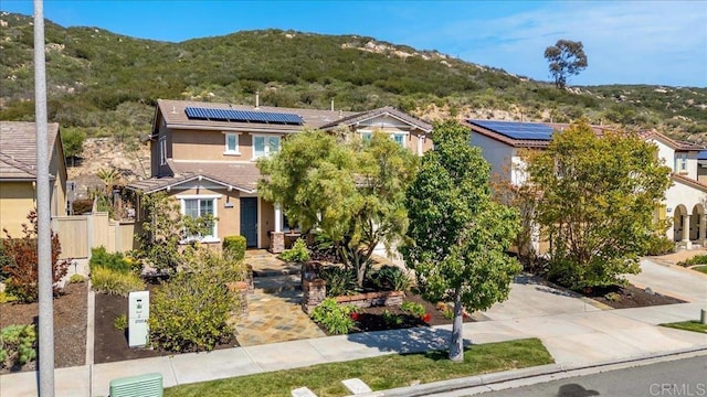view of front facade with a mountain view, stucco siding, solar panels, and a tiled roof