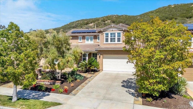 view of front facade featuring a mountain view, concrete driveway, stucco siding, a garage, and roof mounted solar panels
