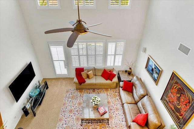living room featuring a towering ceiling, a ceiling fan, healthy amount of natural light, and carpet flooring