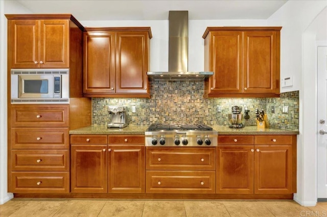 kitchen with appliances with stainless steel finishes, wall chimney exhaust hood, backsplash, and light stone counters