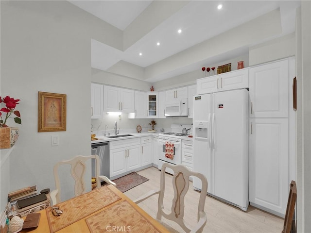 kitchen featuring white appliances, a sink, white cabinets, light countertops, and recessed lighting