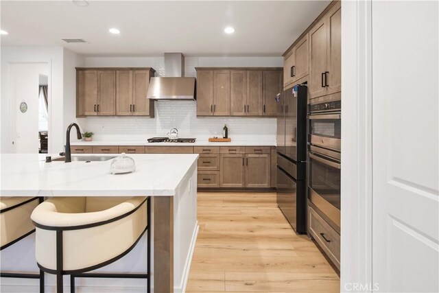 18100 Tableau Way, Saugus, CA 91350 - kitchen featuring freestanding refrigerator, wall chimney range hood, a sink, light wood-style floors, and a breakfast bar area