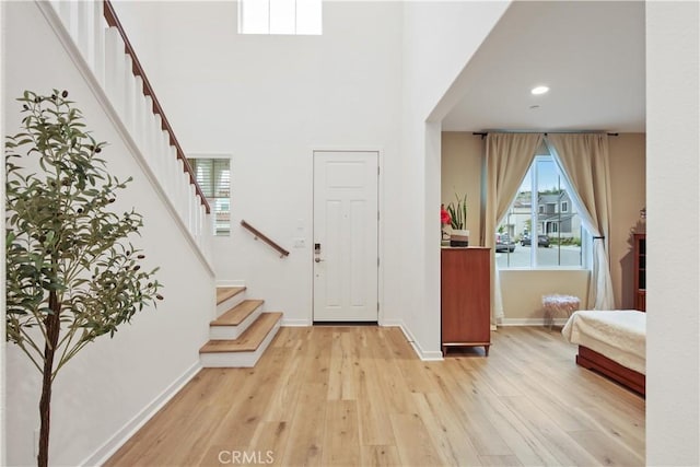foyer entrance with wood finished floors, stairway, healthy amount of natural light, baseboards, and a towering ceiling