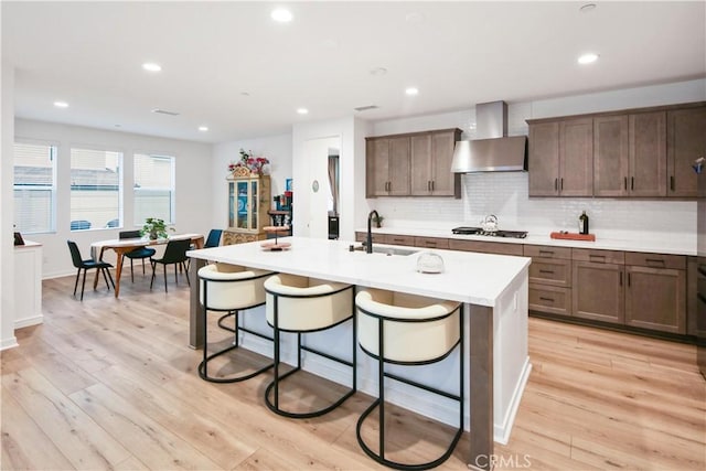kitchen featuring wall chimney range hood, a sink, stainless steel gas cooktop, a breakfast bar area, and recessed lighting