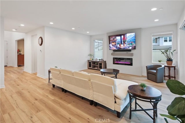 living room with a glass covered fireplace, recessed lighting, light wood finished floors, and baseboards