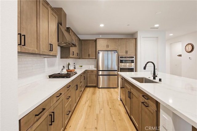 kitchen featuring appliances with stainless steel finishes, wall chimney range hood, a sink, recessed lighting, and light wood-style floors