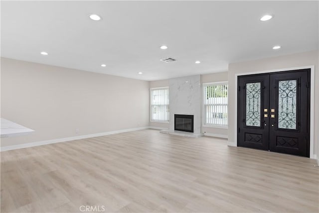 unfurnished living room featuring recessed lighting, light wood-style flooring, french doors, baseboards, and a premium fireplace