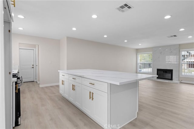 kitchen with light wood-style floors, recessed lighting, white cabinetry, a kitchen island, and a high end fireplace