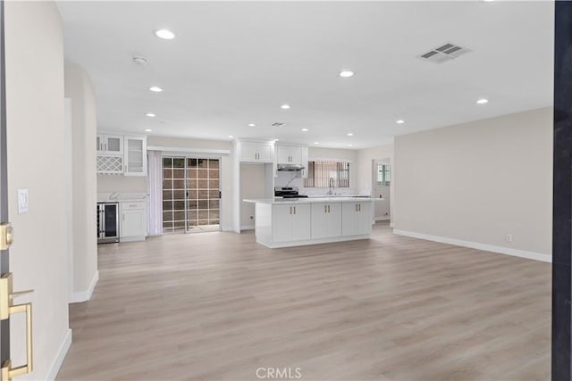 unfurnished living room with wine cooler, baseboards, recessed lighting, light wood-style flooring, and a sink